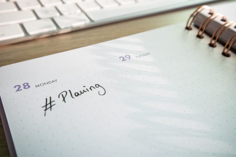 Desk with a keyboard and a planner with the hashtag #planning on it