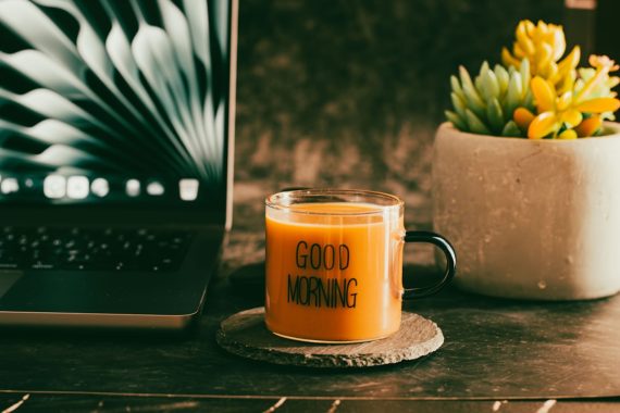 A glass mug with "good morning" text and a laptop.