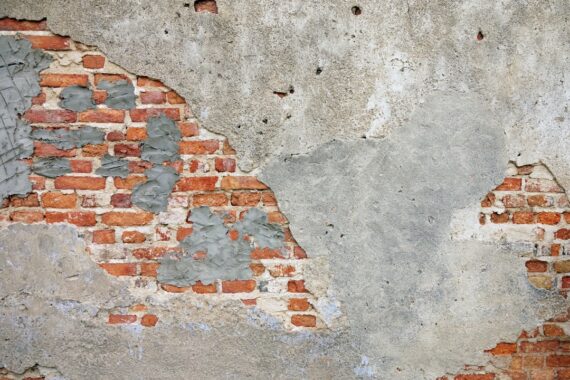 A stuccoed wall where the surface render has fallen away, exposing sound brickwork underneath