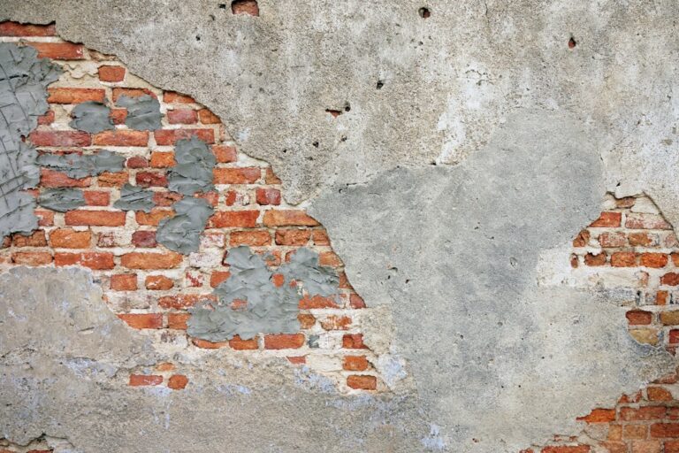 A stuccoed wall where the surface render has fallen away, exposing sound brickwork underneath