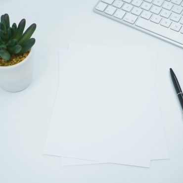 White papers lying on an office desk next to pen,keyboard and small pot flower. Great mockup shot for showcasing a document or print design